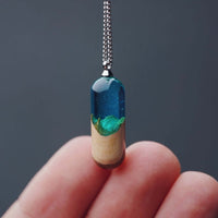 Handcrafted log resin pendant with real log encased in clear resin, held by fingers against a dark background.