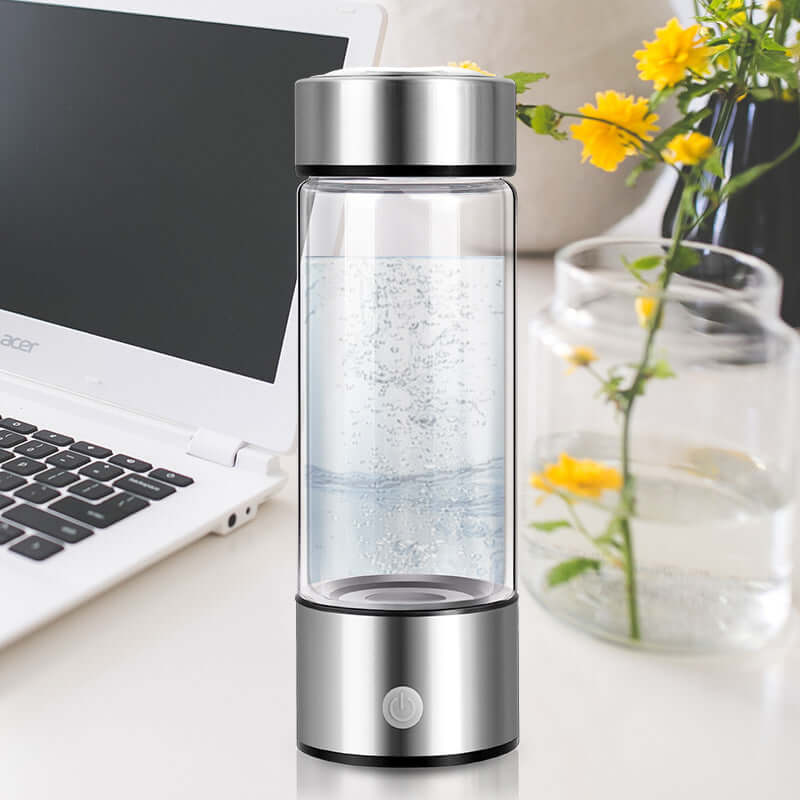 Upgraded Health Smart Hydrogen Water Cup for advanced hydration placed on a desk next to a laptop and flowers.