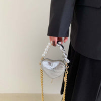 Hand holding Mini Love-Shape Pearls Handbag with a playful heart design, featuring golden chain and pearl details for a cute and functional style.