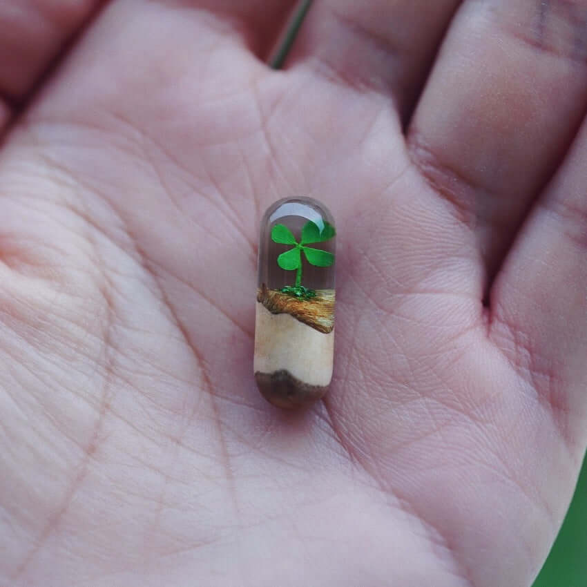 Handcrafted log resin pendant with green clover design in clear resin held in a person's hand