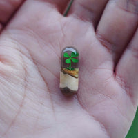 Handcrafted log resin pendant with green clover design in clear resin held in a person's hand